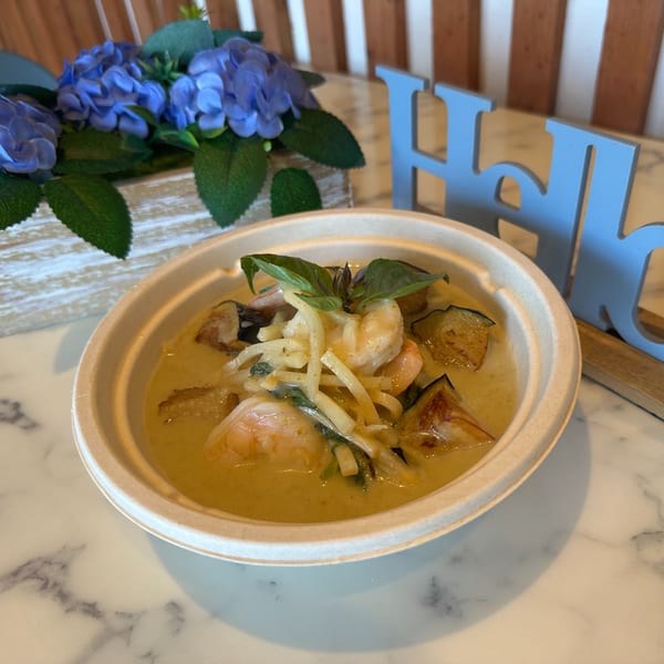 Gen Thai Street Food's green curry with shrimp and eggplant, garnished with basil, on a marble table.