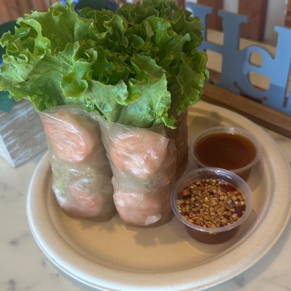 Two fresh spring rolls with lettuce and shrimp, served with two dipping sauces on a white plate.