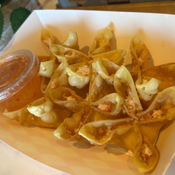 Golden-fried crab rangoon in a white paper tray with a side of sweet chili dipping sauce.